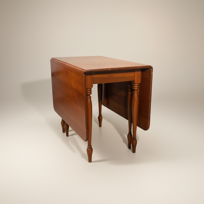 Mesa de comedor estilo Sheraton de madera de cerezo con alas abatibles y patas torneadas, la mesa está con piquetes y rayones – Go Vintage